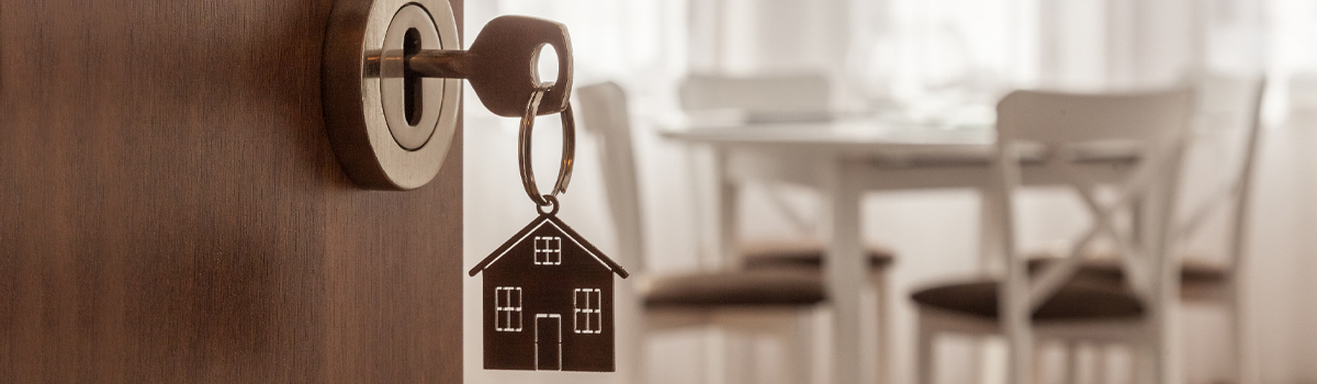 Key with house shaped keychain in an open door to a new home