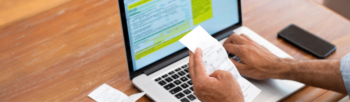 Person holding a receipt in front of a laptop computer.