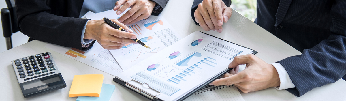 Banker explaining charts and graphs to customer at a desk with a calculator