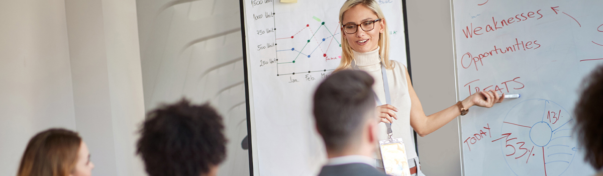 young woman presenting at a whiteboard to a group of people