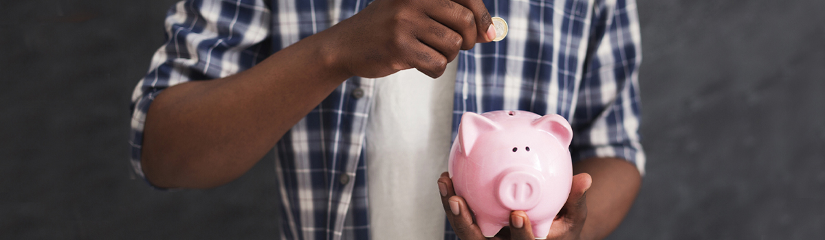 Black man putting a coin into a piggy bank.