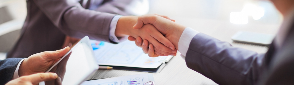 Customer and Banker Shaking hands over a desk with charts and graphs on it