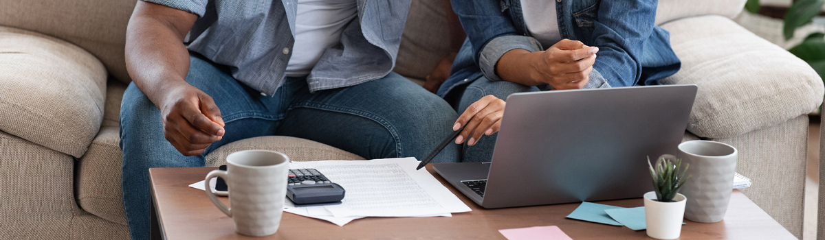 A man and woman sitting on a couch together, online banking on a laptop computer.