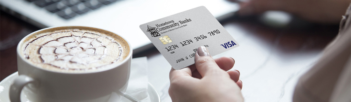 Person holding Hometown Bank Rewards credit card by fancy coffee and laptop