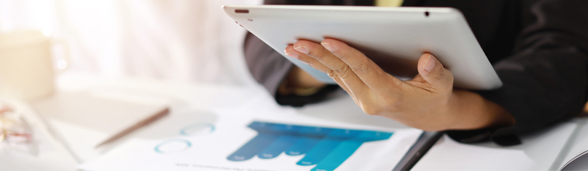 Person working on tablet at desk covered with charts and graphs