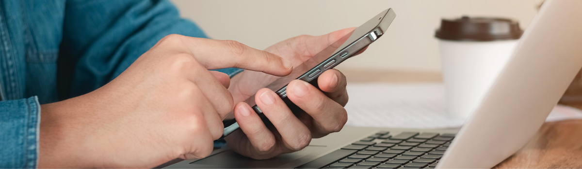 close up of someone setting alerts on their smartphone by a laptop