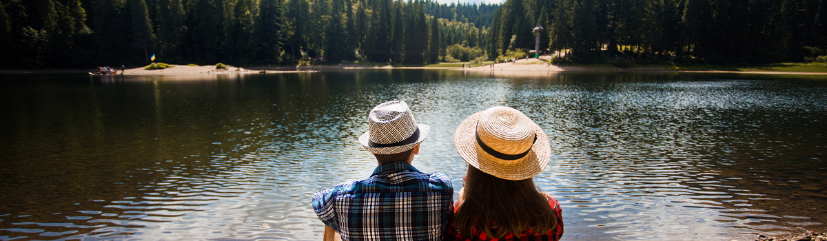 A couple sitting next to each other in front of a lake, surrounded by trees.