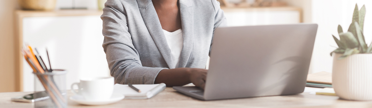 woman at desk working on laptop with notebook and coffee