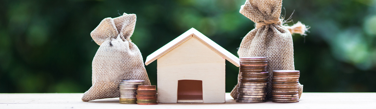 A wooden house sitting next to stacks and bags of coins.