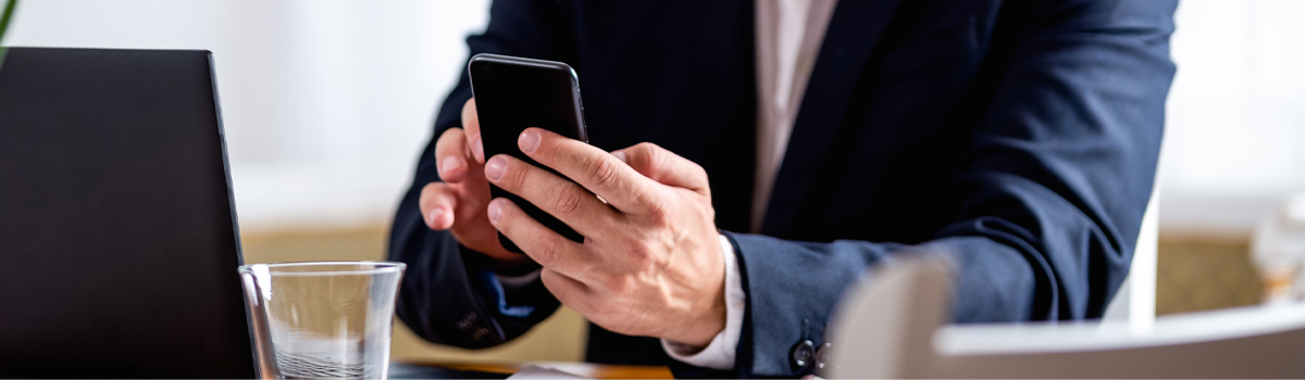 person typing on a smartphone at desk with laptop and glass of water