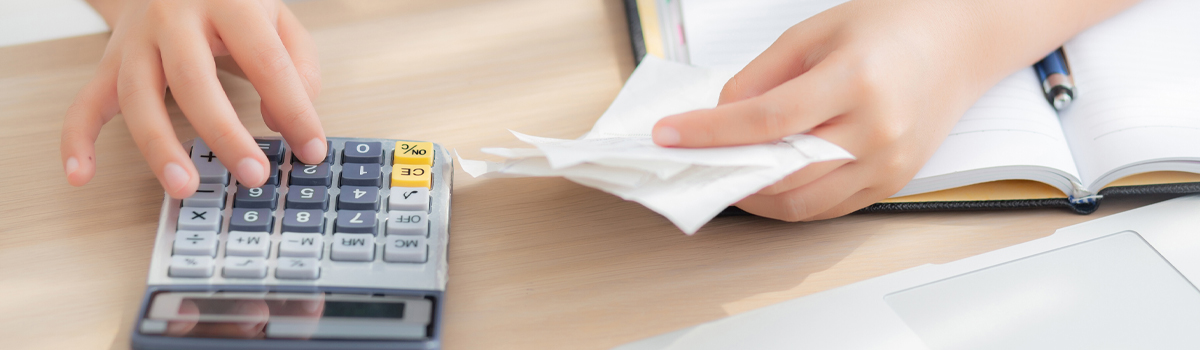 Woman holding a receipt and using a calculator at a desk.